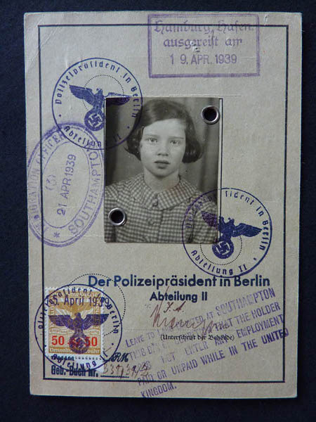 AK: Travel document, 1938. "Well this is my exit card from Germany, as well as my entry card to England, Southampton. At the top, you'll notice the stamp. Hamburg, from where I left Germany on a boat- on a boat called The Manhattan. And it's dated 19th of April 1939 with the German Eagle stamp and then below that there is the English stamp, “landed at Southampton” with my photograph. And then at the bottom there’s a rather interesting little comment, it says, “Leave to land at Southampton granted to the holder, provided the holder does not enter any employment while in the UK, either paid or unpaid.” Well, it is a bit of a joke because I was then ten years old, so it was I likely to take any employment, paid or unpaid?"