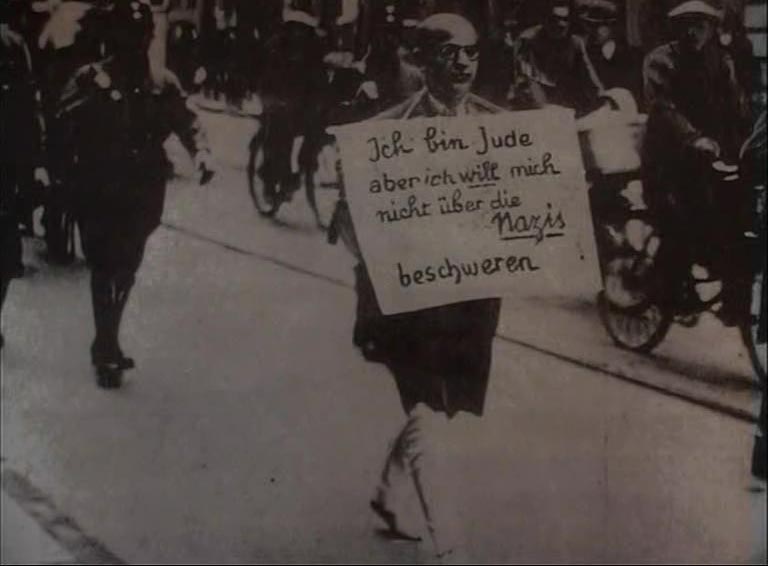 BG: Father Dr. Michael Siegel being marched round Munich after going to the police station to complain on behalf of a Jewish client whose shop had been damaged, Munich, 10th March 1933. "My father had gone to the Police Headquarters to launch a complaint on behalf of a client whose store had been damaged and he’d been taken prisoner. And they said to him, oh Dr. Siegel, you are wanted in room number so-and-so which happened to be in the basement where he found a whole lot of Brownshirts who beat him up and kicked in his teeth, bashed his eardrums, cut off his trouser legs and marched him round Munich like that for an hour maybe, let him go near the main station. Now he never told me this, but he told it to a cousin of mine, they then said ‘go!’ and as he was going they cocked their rifles and said: “Jetzt stirbst du, Jud’!” Now you are going to die, but they never actually fired a shot. So he got into a taxi and a man came up to him and said, look I have just taken some photographs do you mind if I publish them and my father said, do what you like. And that was the photographer... And he sent it off to America, and he was afraid to use it in Germany because apparently the other story is that when Hitler actually got to hear of it he was furious because he did not at that point want that sort of behaviour to be known."