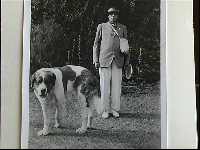 HG: Employer Mr Hunt during a wartime tennis party, with dog, gas mask and tin hat. "This is Mr Hunt at one of the Sunday afternoon tennis parties in the war, with the St Bernard dog, tin hat, gas mask and tennis racket. These afternoons took place quite often"